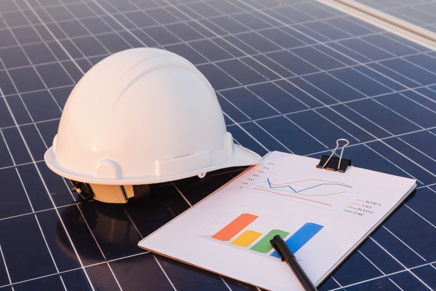 capacete e prancheta com gráficos sobre um painel fotovoltaico para representar o crescimento do mercado de energia solar